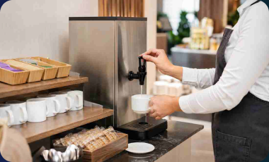 Hospitality staff dispensing hot water from a stainless steel Burco countertop boiler into a mug