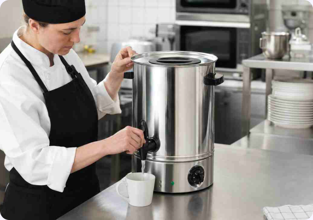 Chef dispensing hot water from a stainless steel Burco boiler into a white mug in a commercial kitchen