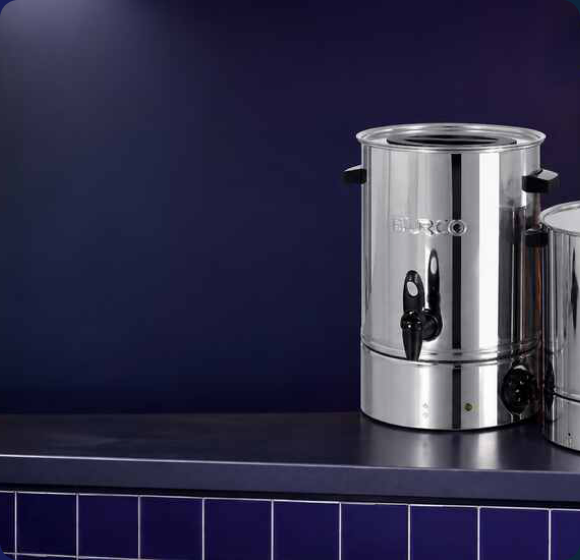 Polished stainless steel Burco commercial water boiler on a dark countertop against a navy wall