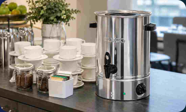 Burco hot water boiler on a dark countertop beside stacked teacups in a hospitality setting