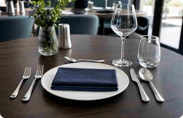 Restaurant table setting with GenWare polished cutlery, white plate, navy napkin and glassware on dark wood