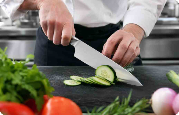 Chef slicing a cucumber with a Global stainless steel chef’s knife in a commercial kitchen