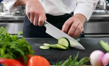 Chef using a Global chef’s knife to slice cucumber on a dark cutting board