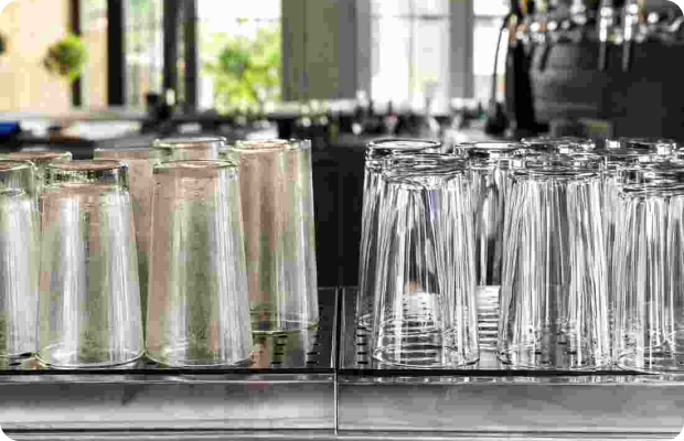 Before and after comparison of cloudy bloomed glasses and crystal-clear glasses on a bar drying rack