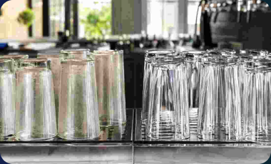 Side-by-side cloudy and sparkling clean drinking glasses on a stainless steel bar rack