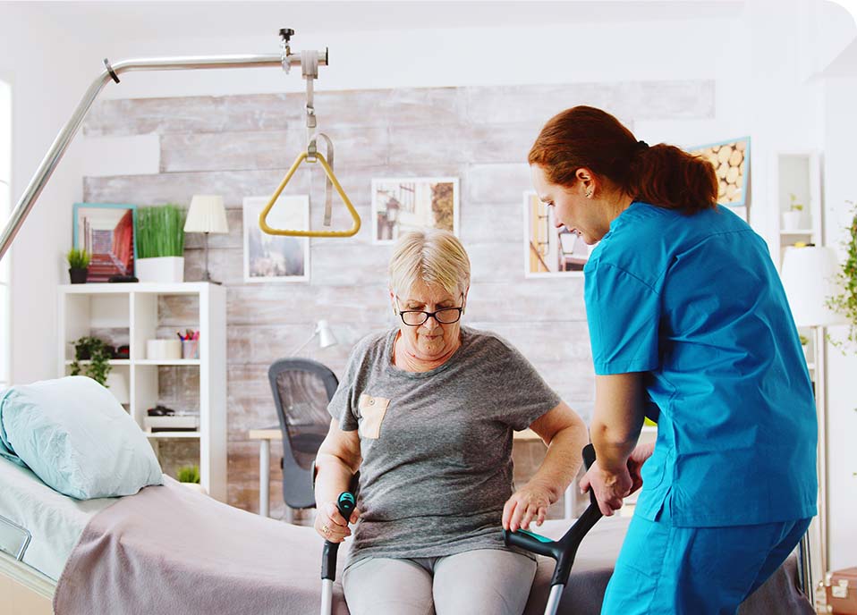 A Care Assistant helps a lady out of a bed